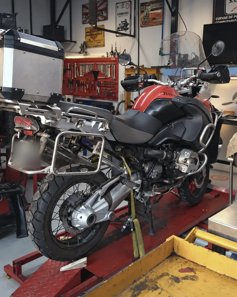 BMW R1200 GS Adventure arriba del elevador, al fondo del taller, con el banco de trabajo al costado.