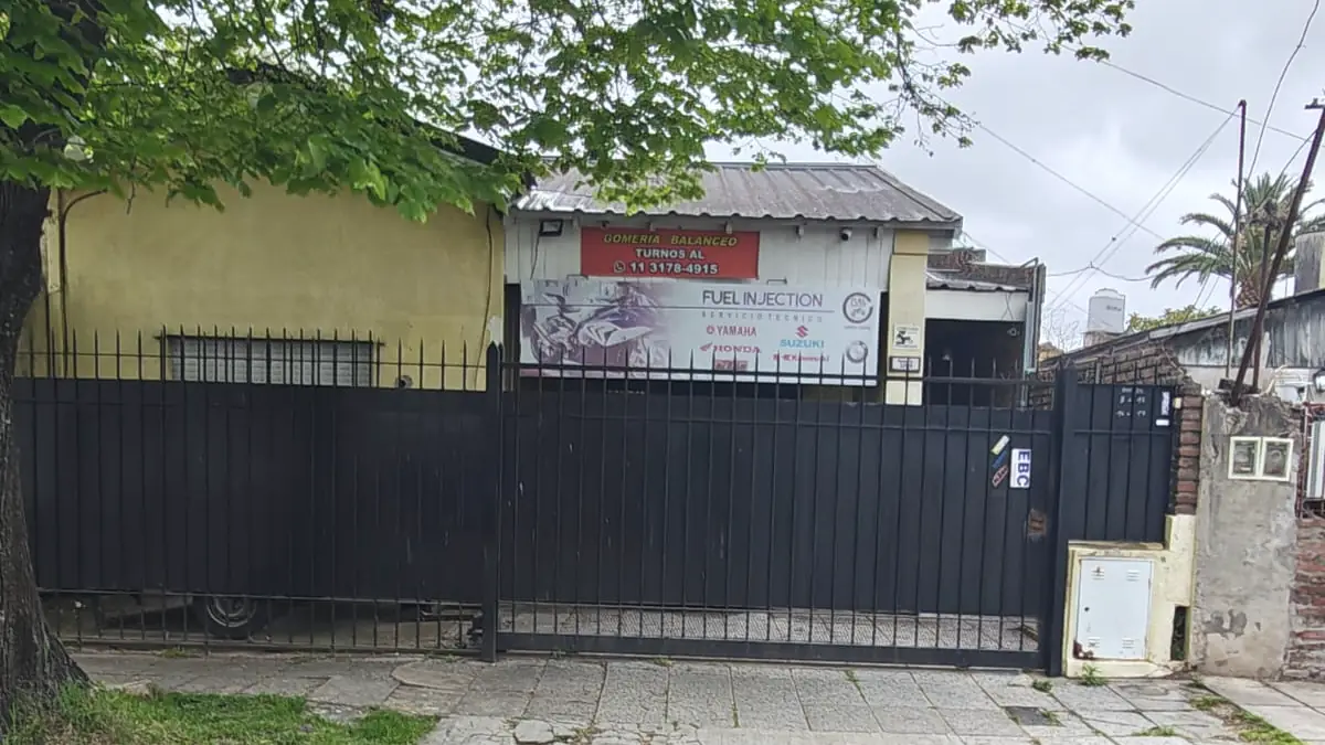 Frente del taller desde la vereda: portón negro, cartel de gomería y balanceo con el teléfono para turnos y cartel de Fuel Injection.