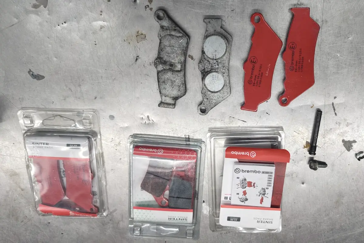 Sobre el banco de metal, las pastillas de freno gastadas al lado de las nuevas, con los blísteres Brembo y los pernos del caliper.