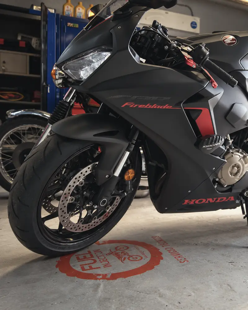 Honda CBR1000RR Fireblade negra en el taller, con el logo de Fuel Injection pintado en el piso.