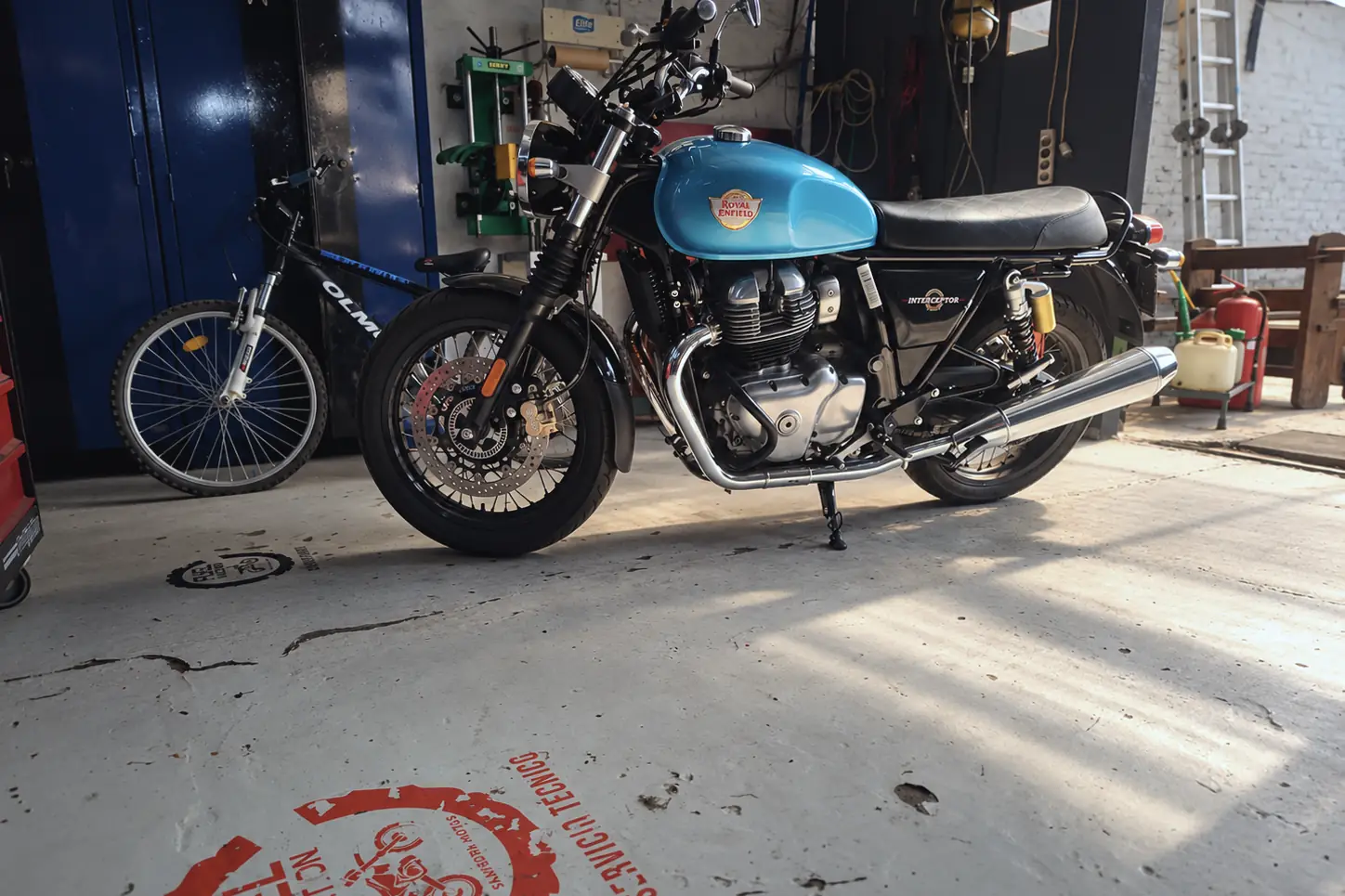 Royal Enfield Interceptor 650 celeste en el taller, con el logo de Fuel Injection pintado en el piso.